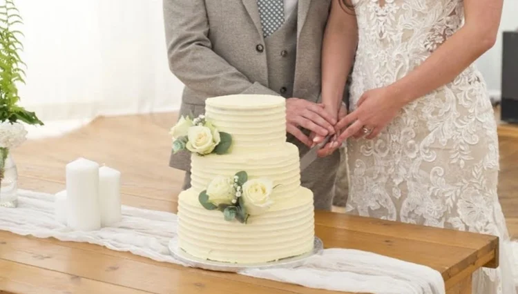 Three-tier white wedding cake with roses being cut at a South Wales wedding venue